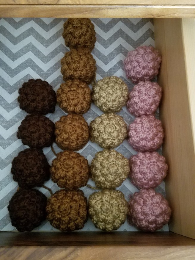 Columns of crocheted hedgehog backs in chocolate, toast, wheat, and rose in a dresser drawer with a gray and white chevron liner.