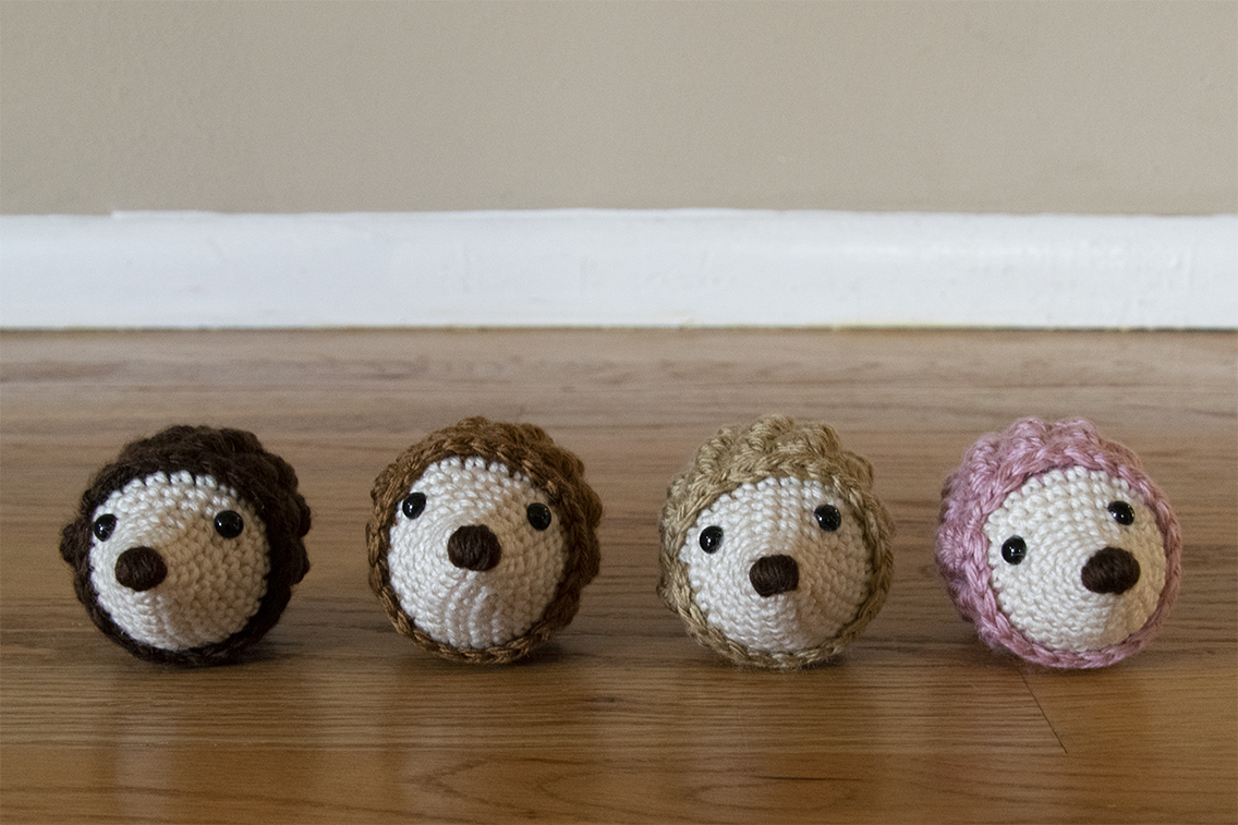A line of four crochet hedgehog amigurumi on a wood floor.
